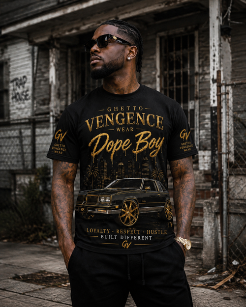 A man wearing a black graphic t-shirt with gold lettering that reads 'Ghetto Vengeance Wear Dope Boy' and a car print, standing in front of a weathered urban building.