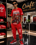 A man modeling a matching red graphic t-shirt and jogger pants set from Ghetto Vengeance Wear inside a modern apparel store. The set features a red graphic tee with 'Ghetto Vengeance' text and a matching pair of red cargo joggers with white and black branding.